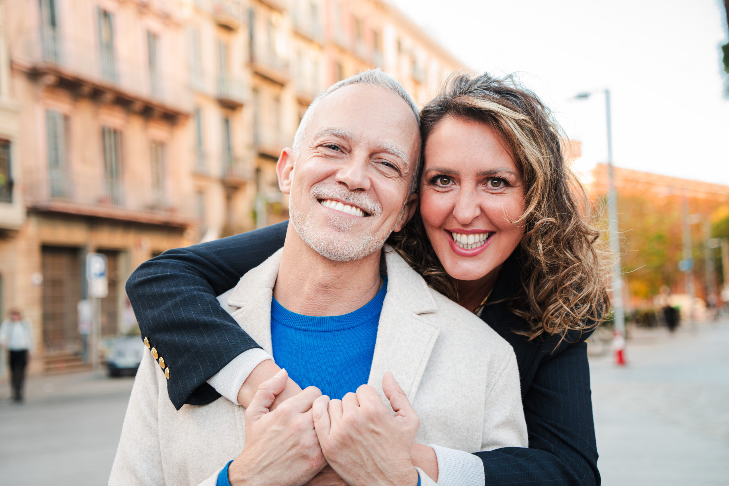 Real mature couple on a relationship smiling together and looking at camera. Mid adult woman embracing her grai hair husband and bonding outside. Middle aged married people enjoying a affectionate hug