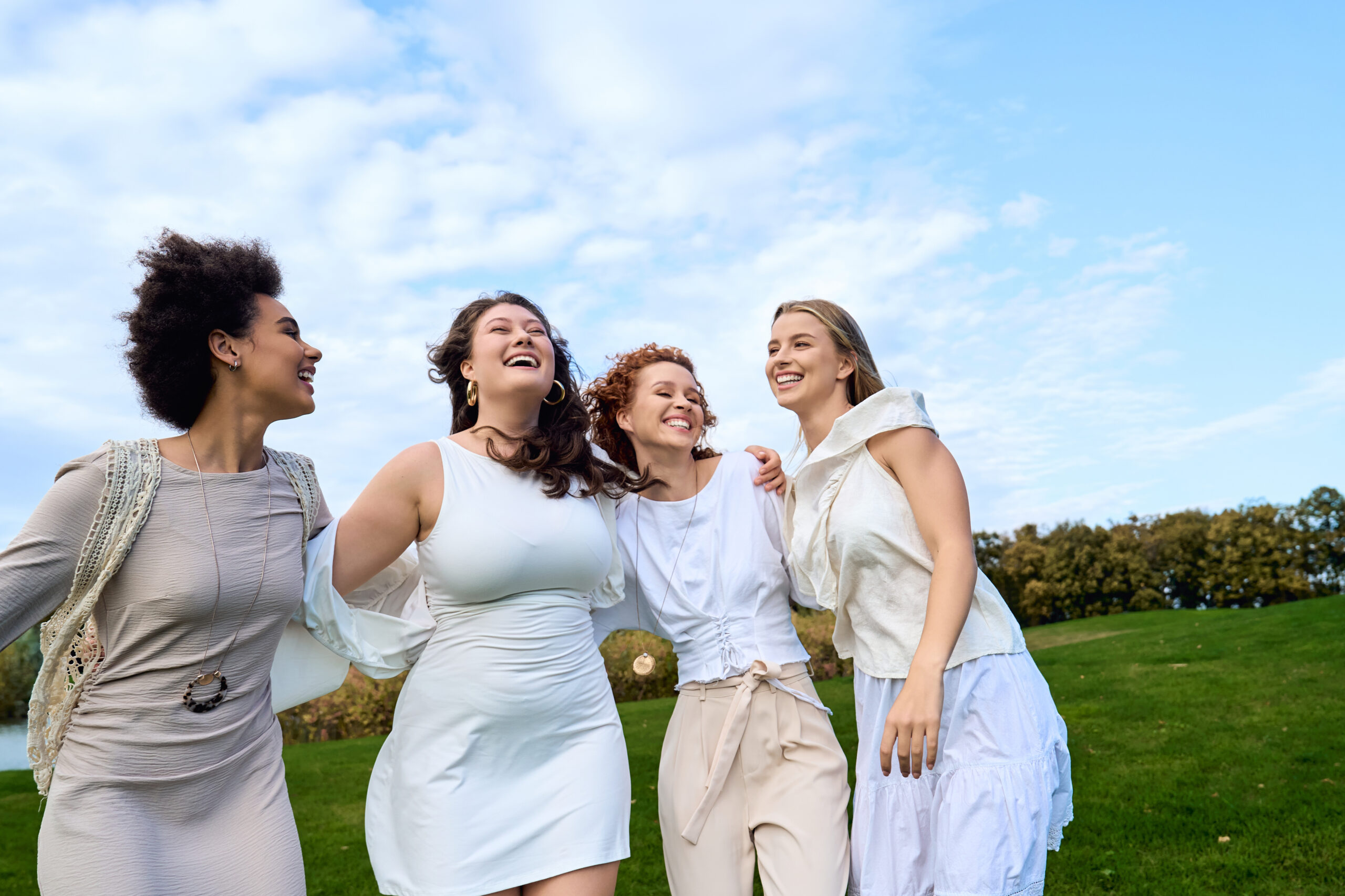 Four fashionable friends joyfully embrace the spring sun while walking in a lush green park.