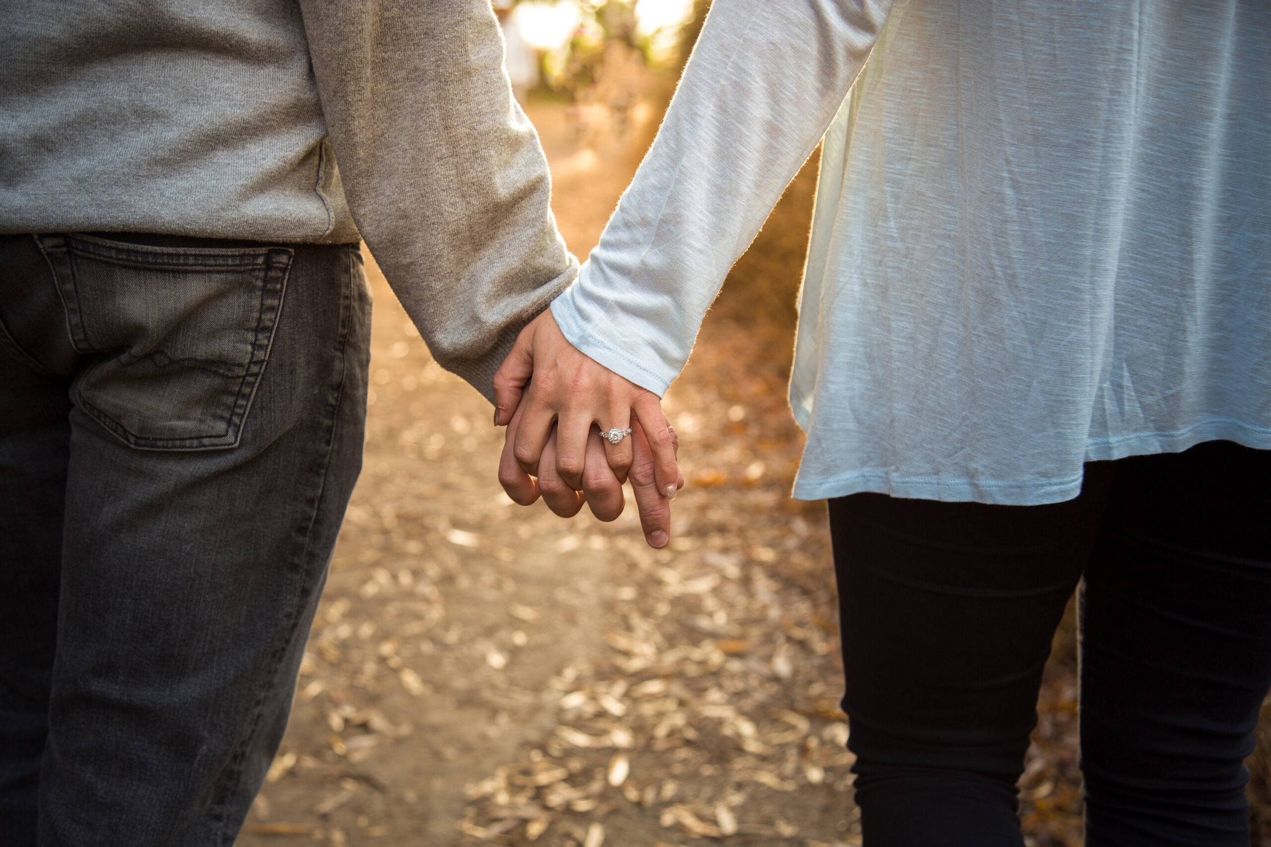 a-couple-holds-hands-as-they-walk-down-a-path-resized