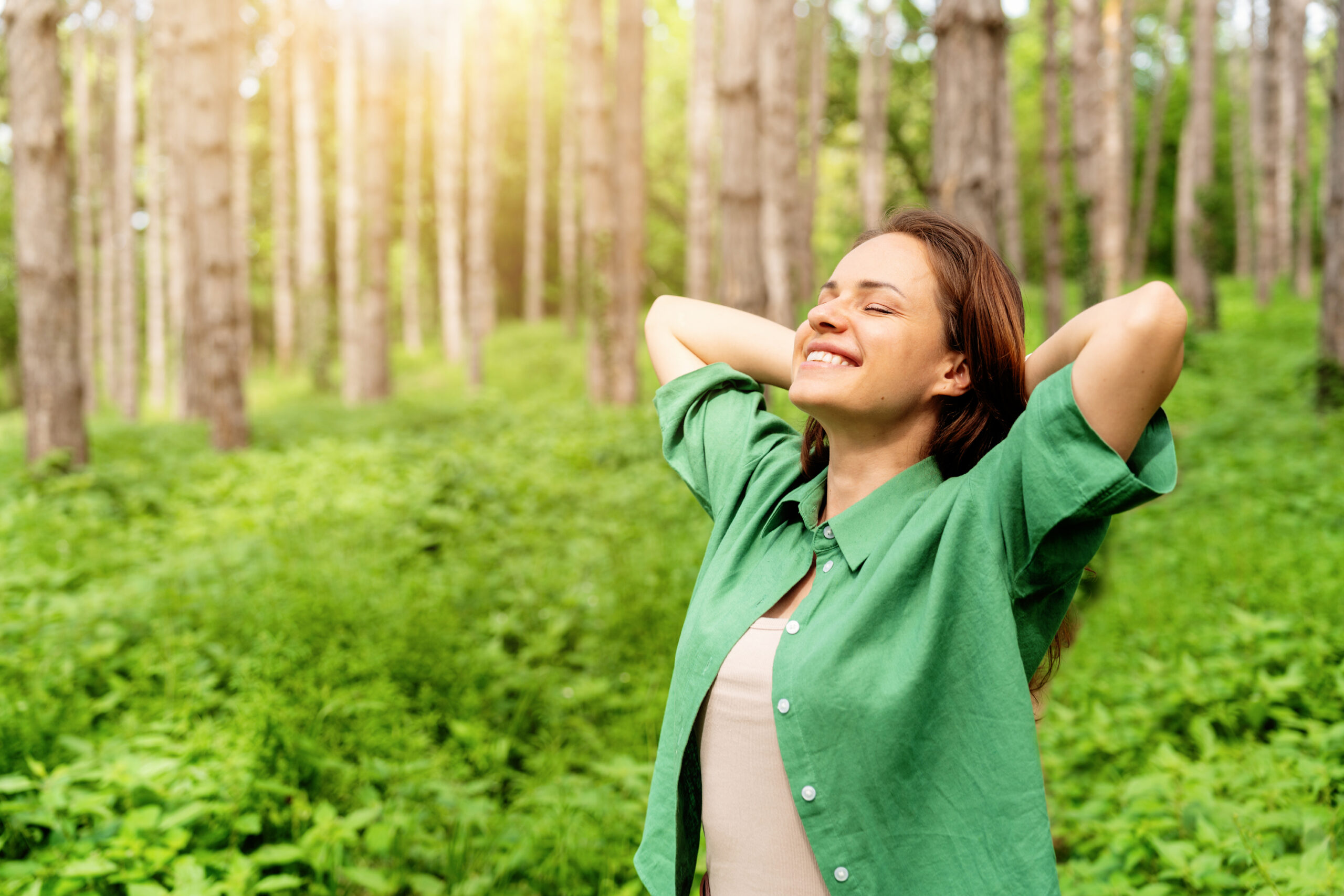 Happy woman standing with hands behind head, enjoying nature in